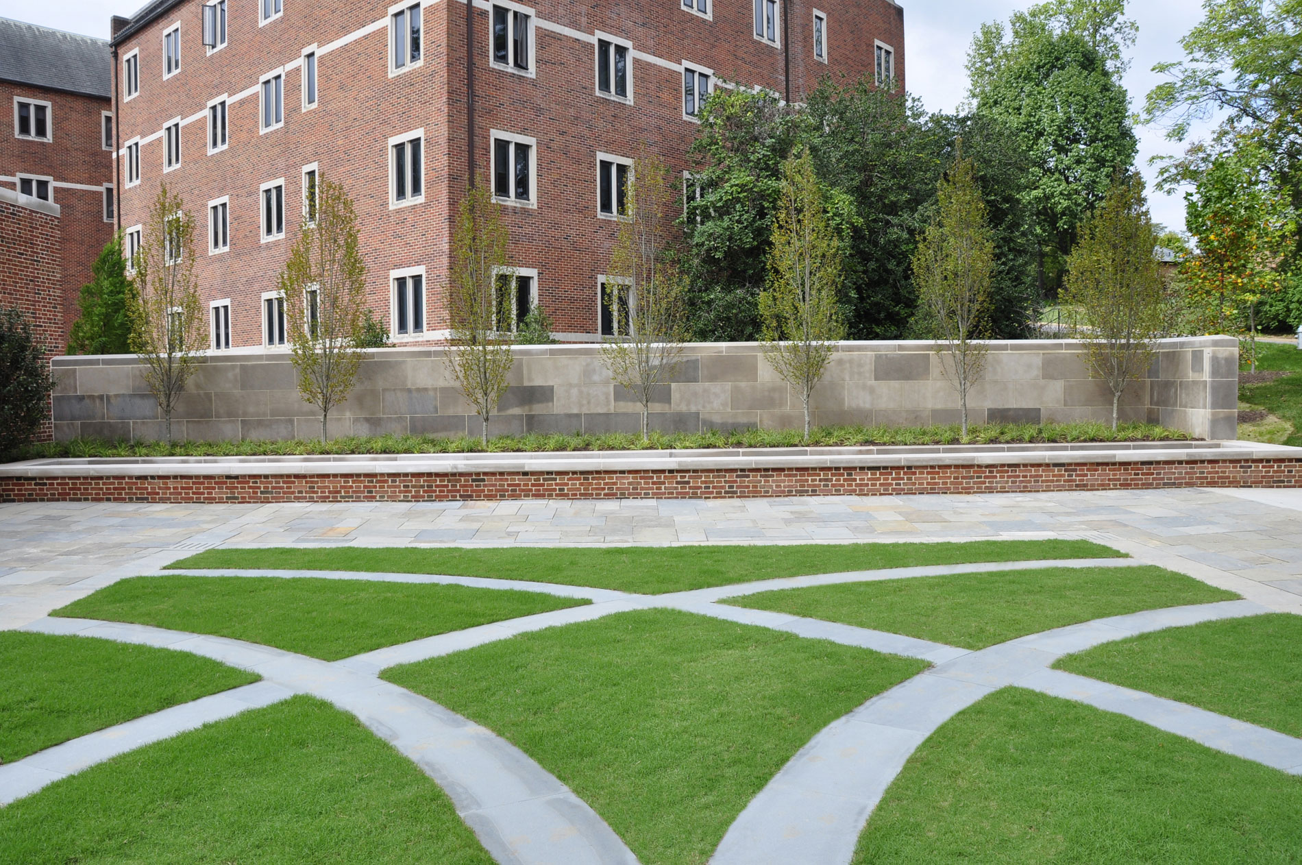 View from within the courtyard looking across the grass panel to the fountain, which is contained by a brick seat wall. Behind the fountain a planting of Fastigiate Hornbeam will eventually form an aerial hedge that will be clipped above the height of the limestone wall behind and create a greater sense of enclosure on this edge of the courtyard.